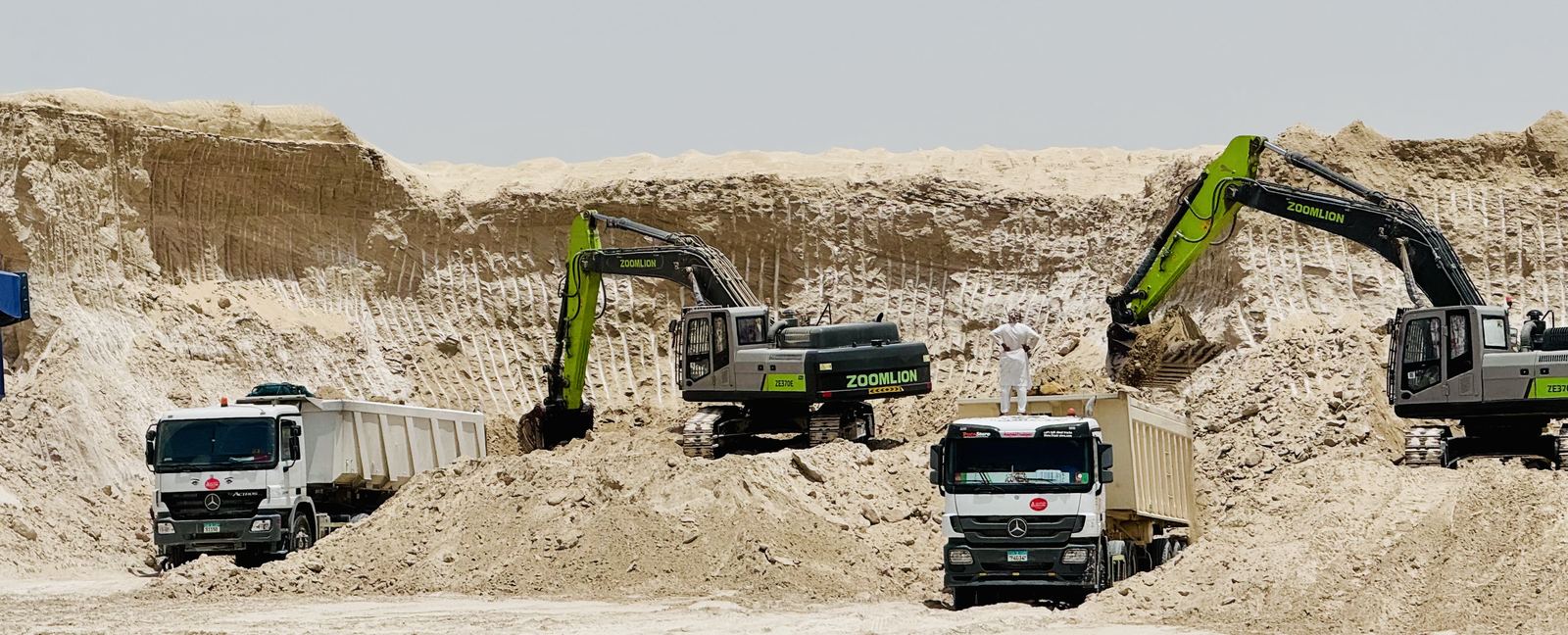 Two excavators loading tipper trucks at a borrow pit